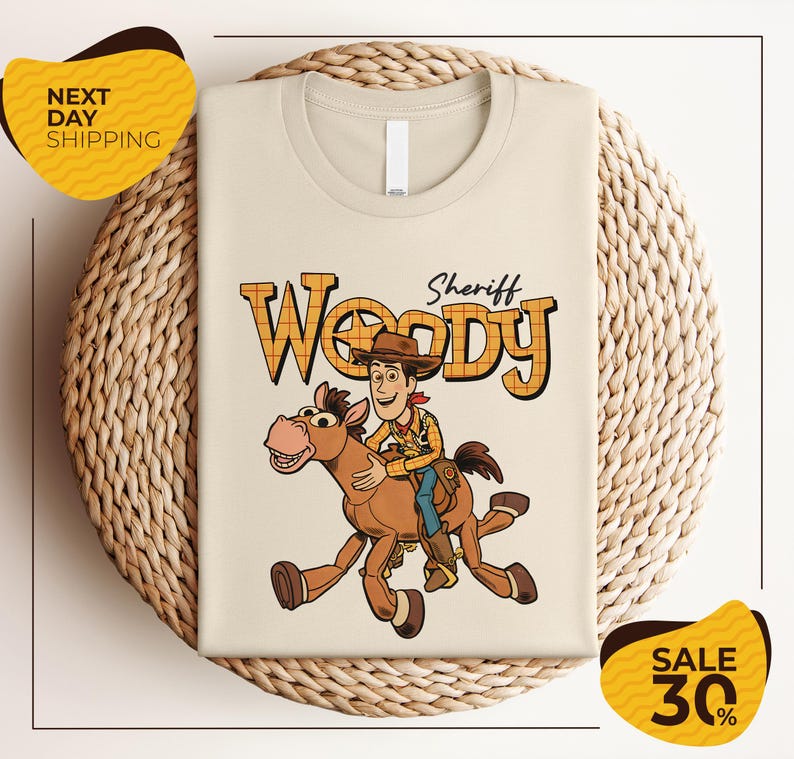 A t-shirt featuring a cartoon image of Woody, a character from the Toy Story franchise, riding a horse. The t-shirt is displayed on a woven basket, and there are two yellow sale signs indicating a 30% discount on the item.