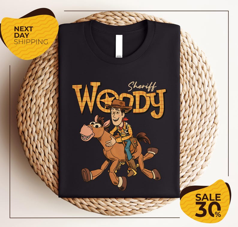A black t-shirt with a cartoon image of Woody, a character from the Toy Story franchise, riding a brown horse. The t-shirt is displayed on a woven basket, and there are yellow price tags indicating a sale of 30% off.