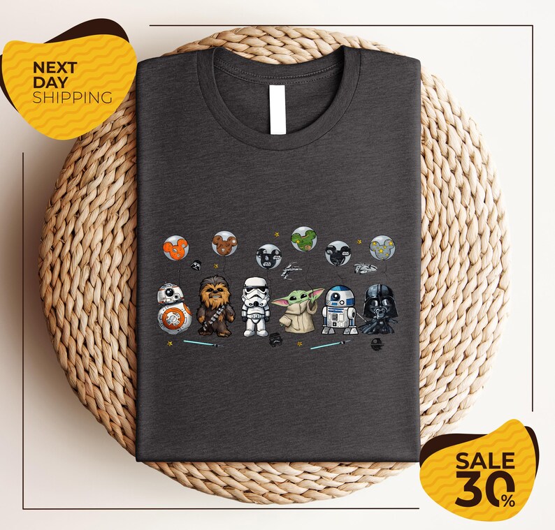 a gray t-shirt with a graphic design of various Star Wars characters, including Chewbacca, Stormtrooper, Darth Vader, and Baby Yoda, arranged in a row.