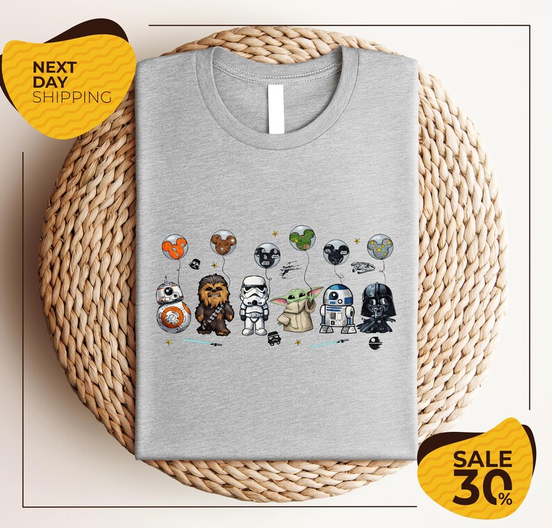 A gray t-shirt with a graphic design featuring various Star Wars characters, including Chewbacca, Stormtrooper, Darth Vader, and Baby Yoda, along with balloons.