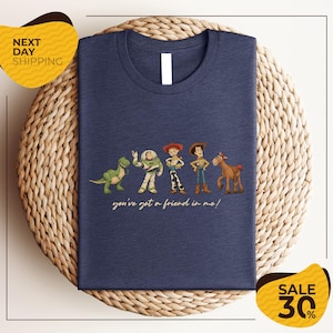 A blue t-shirt with a graphic design featuring characters from the Toy Story movie, including Woody, Buzz Lightyear, and a dinosaur. The text on the t-shirt says "you've got a friend in me!"