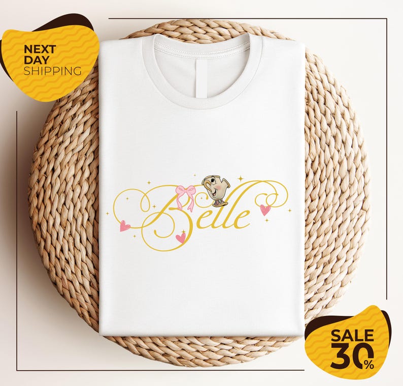 a white t-shirt with a printed design, including the word "Belle" and decorative elements such as hearts and a bow. The t-shirt is displayed on a woven basket, and there are two yellow sale signs in the image, one on the left and one on the right, indicating a sale or discount.