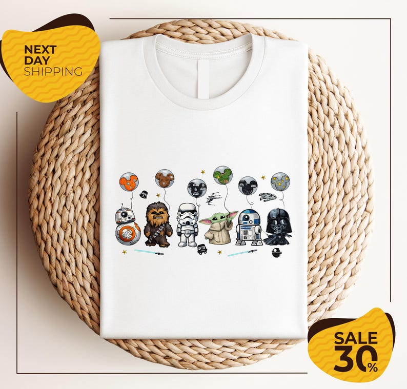 A white t-shirt with a graphic design featuring various Star Wars characters, including Chewbacca, Stormtrooper, Darth Vader, and Baby Yoda, along with other Star Wars-themed elements.