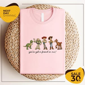A pink t-shirt with a graphic design featuring characters from the Toy Story movie, including Woody, Buzz Lightyear, and a horse. The text below the characters says "you've got a friend in me!"