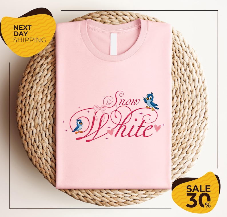 A pink t-shirt with the text "Snow White" and two blue birds, placed on a woven basket.
