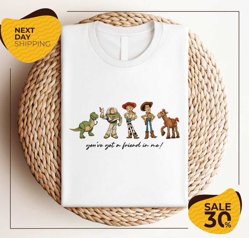 A white t-shirt with a graphic design featuring characters from the Toy Story movie, including Woody, Buzz Lightyear, and a horse. The text below the characters says "you've got a friend in me!"