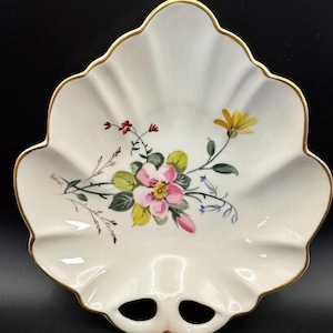 May include: A white porcelain dish shaped like a leaf with a scalloped edge and gold trim. The center features a hand-painted floral arrangement with a pink rose, yellow daisy, and green leaves. The signature Challinor is visible on the left side.