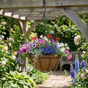 Puede incluir: Una cesta colgante llena de flores coloridas, incluyendo flores rojas, rosas, moradas, azules y blancas. La cesta está suspendida de una cadena y un gancho negros, sobre un fondo de jardín con una pérgola de madera.