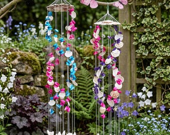 May include: Two seashell wind chimes hanging from a tree branch. One chime features pink and blue shells, the other has pink and purple shells. The chimes are suspended by clear strings. Pink butterflies are perched on the branch above.