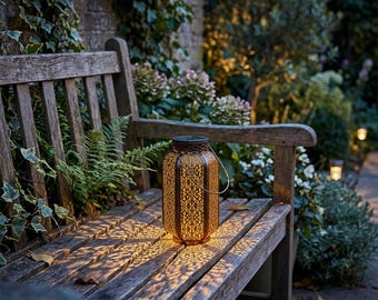 May include: A decorative bronze-colored lantern with an intricate pattern sits on a wooden bench. The lantern casts a warm, patterned light onto the bench. The scene is set outdoors with greenery in the background, suggesting garden decor.