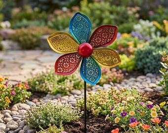 May include: A colorful metal flower garden stake with a red, yellow, and blue design. The flower has intricate cut-out patterns and a red center. The stake is in a garden bed with various flowers and greenery.
