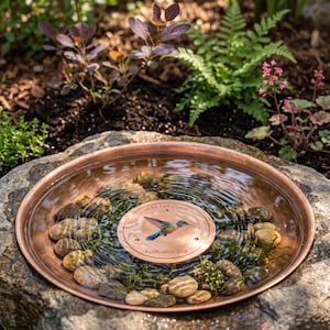 Peut inclure: Un bassin rond en cuivre rempli d'eau et de galets lisses. Au centre se trouve un disque de purification en cuivre circulaire orné d'une illustration de colibri coloré et du texte 99.9% Pure Copper Purification Disk.