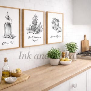 Op de afbeelding: Drie ingelijste zwart-wit botanische prenten hangen boven een houten aanrecht in een keuken. De prenten tonen olijfolie, basilicum rozemarijn tijm en citroenen en knoflook. Een snijplank, planten en keukengerei zijn ook zichtbaar.
