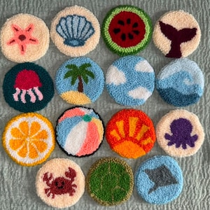 May include: A collection of fourteen circular punch needle coasters featuring various summer-themed designs including a starfish, seashell, watermelon slice, whale tail, jellyfish, palm tree, clouds, ocean waves, orange slice, beach ball, sun, octopus, crab, turtle, and stingray.