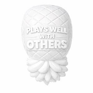 May include: A white pineapple-shaped ornament with a textured surface and the words "PLAYS WELL WITH OTHERS" in raised lettering. The pineapple has a diamond pattern on the top and a detailed base.