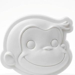 Könnte beinhalten: Eine weiße, dreidimensionale Skulptur eines lächelnden Affengesichts. Der Affe hat große, runde Augen, eine kleine Nase und einen breiten, gebogenen Mund. Die Skulptur ist glatt und hat eine matte Oberfläche. Die Ohren und Haare des Affen sind ebenfalls sichtbar.