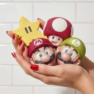 Könnte beinhalten: Eine Sammlung bunter Badebomben in Form von Charakteren aus der Super Mario-Videospielserie. Enthält einen gelben Stern, einen rot-weißen Pilz sowie Mario- und Luigi-Köpfe.