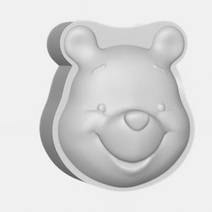 May include: A grey, three-dimensional Winnie the Pooh face. The bear's smiling face is in a rounded square shape, with two small ears at the top. The nose is a small oval, and the eyes are small ovals.