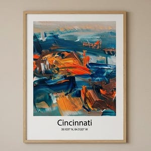 Puede incluir: Un cuadro enmarcado con una pintura abstracta vibrante en tonos azules, naranjas y marrones. La palabra "Cincinnati" está impresa debajo de la obra de arte, junto con las coordenadas 39.1032° N, 84.5120° W.