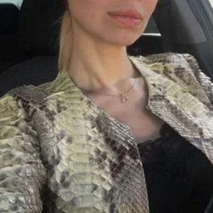 May include: A jacket featuring a textured snakeskin pattern in shades of beige, cream, and dark brown. The garment has a structured collarless neckline and is worn over a black top with lace trim. A thin gold chain necklace with a small pendant is visible.