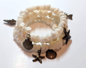 May include: A white shell bead bracelet with multiple charms, including seashells and starfish. The charms are made of metal and have a bronze finish.