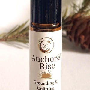 May include: A small, brown glass roller bottle with a black cap. The label reads "Anchor & Rise" with the words "Grounding & Uplifting" below. The bottle contains 10 ml of product.