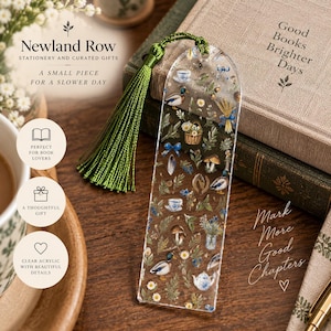 May include: A clear acrylic bookmark featuring a printed pattern of mallard ducks, mushrooms, teacups, floral arrangements, and blue ribbons. The bookmark has a rounded top with a hole and a long, dark green silk tassel attached to the top.