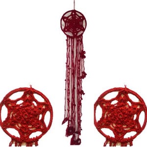 Puede incluir: Atrapasueños de ganchillo rojo con un centro en forma de estrella y borlas colgantes. El atrapasueños está hecho a mano y presenta un diseño circular con intrincados calados. También se ven dos piezas de ganchillo adicionales en forma de estrella a juego.