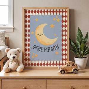 May include: A framed wall art print featuring a light blue background with a smiling yellow crescent moon and several yellow stars. The text OÍCHE MHAITH is printed in black below the moon. The frame has a red and white diamond pattern border.