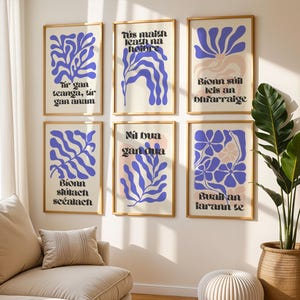 Op de afbeelding: Zes ingelijste kunstprints met botanische ontwerpen in blauw en roze op een crèmekleurige achtergrond. Elke print heeft een gouden lijst en bevat tekst in een gestileerd lettertype. De prints worden tentoongesteld aan een witte muur boven een beige bank.