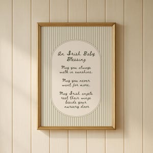 Könnte beinhalten: Ein gerahmter Druck mit dem Text "An Irish Baby Blessing". Der Hintergrund hat vertikale beige und hellgraue Streifen, mit dem Text in einem ovalen Rahmen. Der Rahmen ist goldfarben.