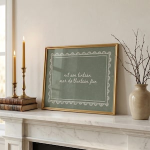 Può includere: Una stampa artistica rettangolare in una cornice dorata con sfondo verde salvia, un bordo bianco in stile pizzo e il testo corsivo bianco "nil aon tintean mar do thintean fein" centrato all'interno della cornice decorativa.
