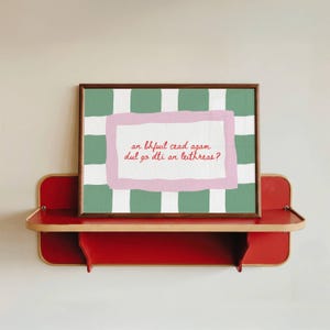 Puede incluir: Una impresión enmarcada con un fondo a cuadros verdes y blancos y un marco interior rosa y blanco. El texto en el marco interior es rojo. La impresión se muestra en un estante rojo.