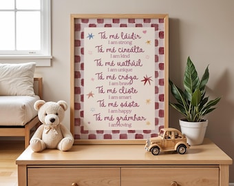 May include: A framed wall art print featuring a red and white checkered border and a list of positive affirmations in Irish and English. The text includes phrases like Tá mé láidir, I am strong, Tá mé cineálta, I am kind, and other similar statements.