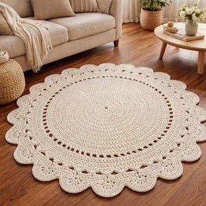 May include: A cream-colored, round crochet rug with a scalloped edge. The rug is placed on a hardwood floor in a living room setting. The rug's diameter is approximately 60 inches.