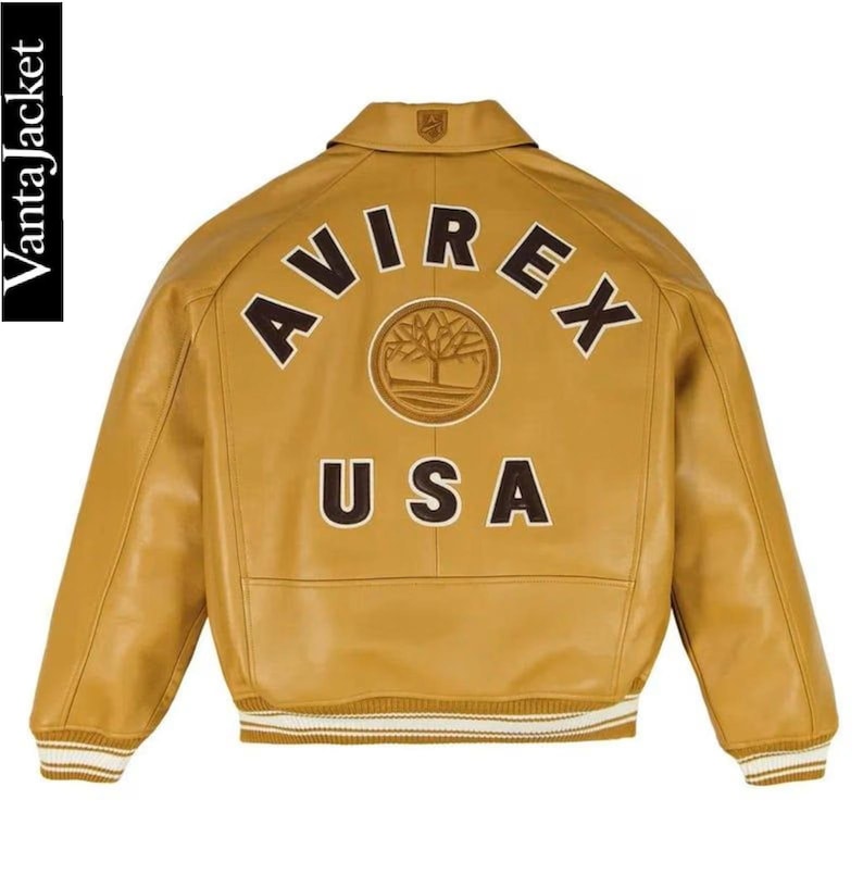 May include: Mustard yellow leather jacket with the word "AVIREX" arched across the back, above "USA". A circular emblem is centered between the words. The jacket has a collared neckline and ribbed cuffs with white stripes.