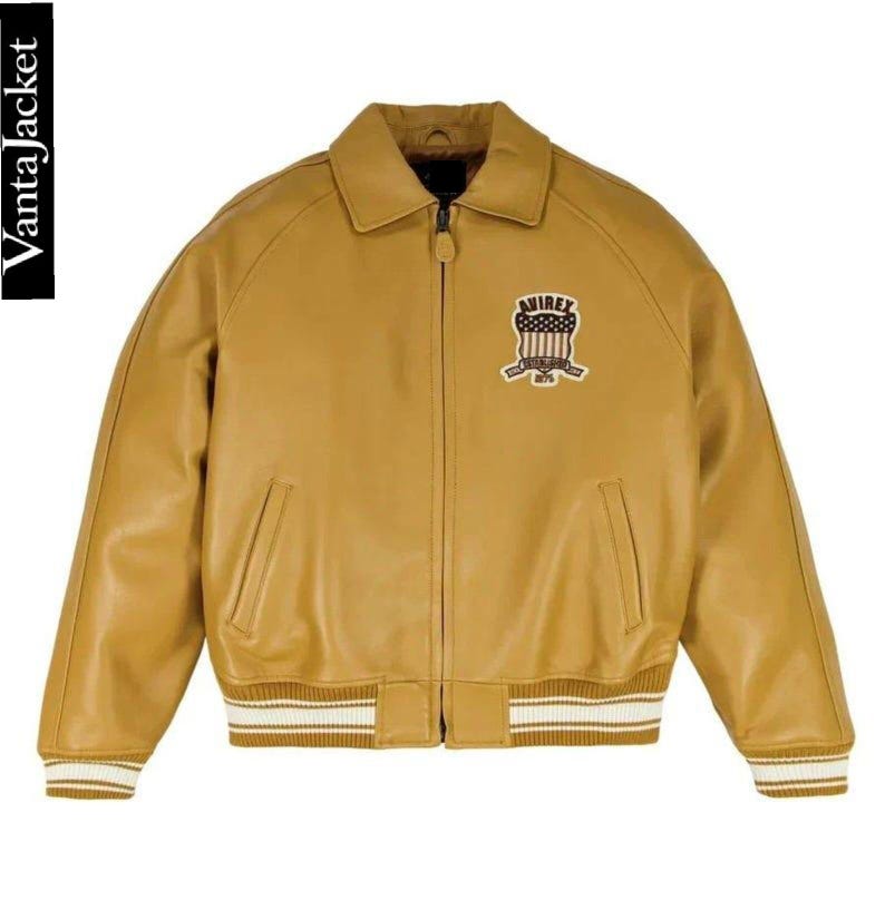 May include: Mustard-colored leather jacket with a zip-up front, collar, and ribbed cuffs and hem. Features a patch on the chest with the text "AVIREX" and an emblem. The jacket has two front pockets and the text "VantaJacket" on the side.