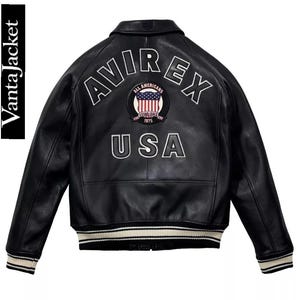 May include: Black leather jacket with white embroidered "AVIREX USA" lettering and a circular patch featuring the American flag. The jacket has a ribbed collar, cuffs, and hem with white and black stripes. The brand name "VantaJacket" is printed vertically on the left side.