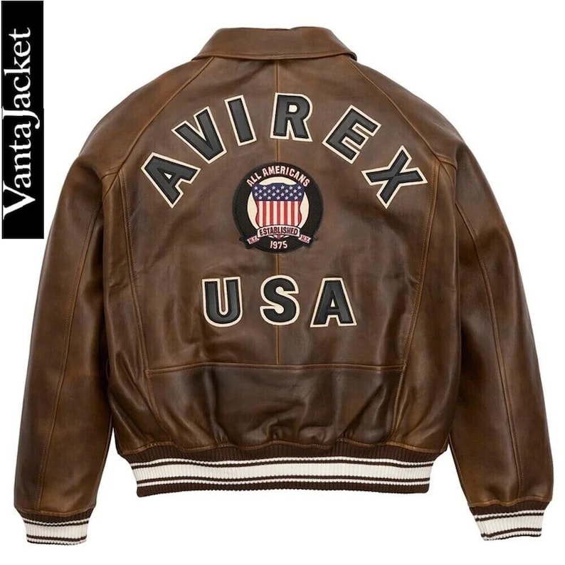May include: Brown leather jacket with the word "AVIREX" across the back in white block letters. Below the word "AVIREX" is a patch with the words "ALL AMERICANS ESTABLISHED 1975" and a USA flag design. The word "USA" is below the patch. The jacket has a white and brown striped trim.