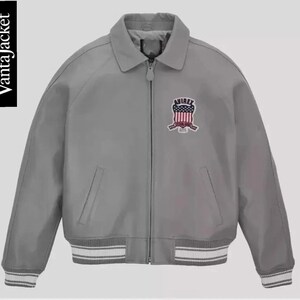 May include: A gray bomber jacket with a collared neckline and a zipper closure. The jacket features a patch on the chest with the text "AVIREX" and a design in red, white, and blue. The cuffs and hem have white and gray striped detailing. The text "VantaJacket" is on the left side.
