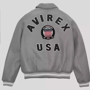 May include: A gray bomber jacket with the word "AVIREX" arched across the back in black letters. Below the word is a circular patch with the words "ALL AMERICANS" and "ESTABLISHED 1975" surrounding a design of the American flag. The word "USA" is below the patch.