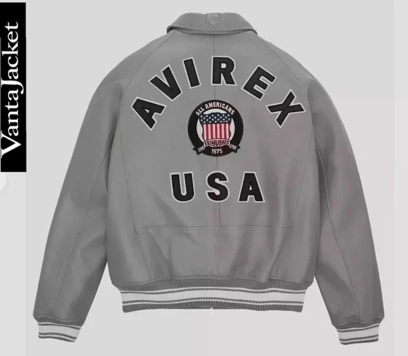 May include: A gray bomber jacket with the word "AVIREX" arched across the back in black letters. Below the word is a circular patch with the words "ALL AMERICANS" and "ESTABLISHED 1975" surrounding a design of the American flag. The word "USA" is below the patch.