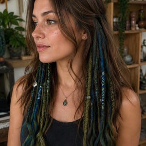 Puede incluir: Un conjunto de extensiones de cabello que presenta una mezcla de mechones en color marrón oscuro, verde bosque y azul profundo. Las extensiones tienen forma de trenzas finas y texturizadas con cuentas metálicas integradas para usar en el cabello.