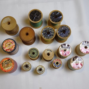 Puede incluir: Una colección de carretes de hilo de madera vintage, algunos con etiquetas de Coats & Clark y otras marcas. Los carretes varían en tamaño y color, con hilos en verde, azul y rosa.