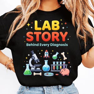 May include: Black t-shirt with the words "LAB STORY" in yellow and red, and the tagline "Behind Every Diagnosis." The shirt features a graphic of lab equipment, including a microscope, beakers, a rocket, and a pink pig.