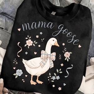 Puede incluir: Sudadera negra con una ilustraci&oacute;n de un ganso blanco con un lazo a cuadros, rodeado de motivos florales y de coraz&oacute;n. Las palabras "mama goose" est&aacute;n escritas encima del ganso en cursiva. Un dise&ntilde;o encantador y caprichoso.