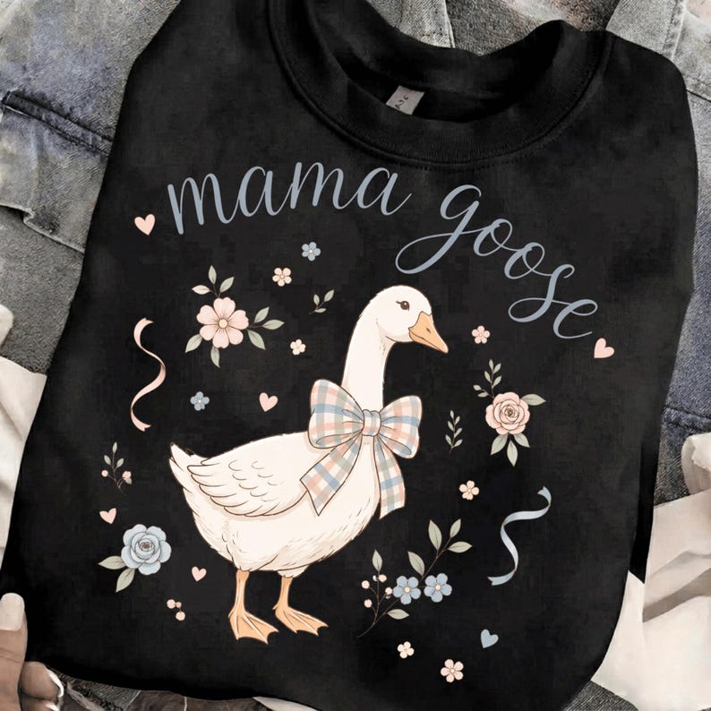 Puede incluir: Sudadera negra con una ilustraci&oacute;n de un ganso blanco con un lazo a cuadros, rodeado de motivos florales y de coraz&oacute;n. Las palabras "mama goose" est&aacute;n escritas encima del ganso en cursiva. Un dise&ntilde;o encantador y caprichoso.