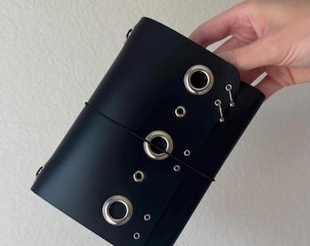 Cuaderno tríptico A6 de cuero negro perforado con ojales y bolsillo, hecho a mano.
