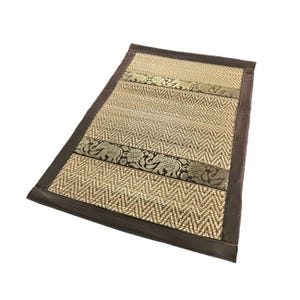 Peut inclure: Tapis rectangulaire tissé avec une bordure marron. Le tapis présente un motif en chevrons beige et marron. Des bandes décoratives avec des motifs d'éléphants et de fleurs en or et noir sont présentes.