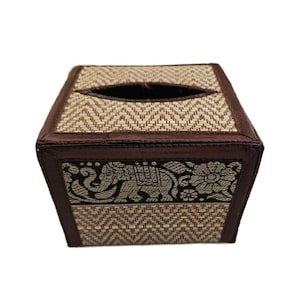 以下が含まれることがあります： ベージュと茶色の織りジグザグ模様の正方形のティッシュボックス。上部には楕円形の開口部があります。下部のボーダーには、象と花のパターンが黒とベージュで施されています。